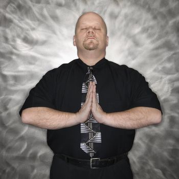 Caucasian bald mid adult men standing with hands together and eyes closed in a meditative position.