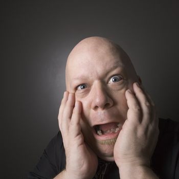 Caucasian mid adult bald man with hands to face making scared facial expression.