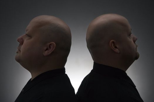 Caucasian mid adult bald identical twin men standing back to back.