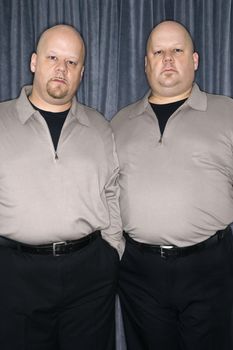 Caucasian bald identical twin mid adult men standing together looking at viewer.