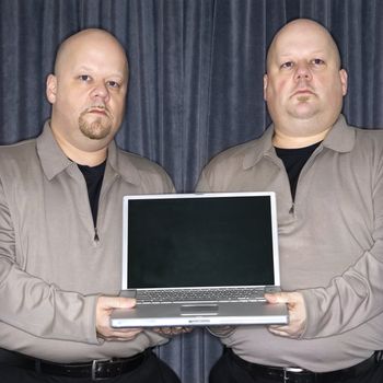 Caucasian bald identical twin men holding a laptop computer and looking at viewer.