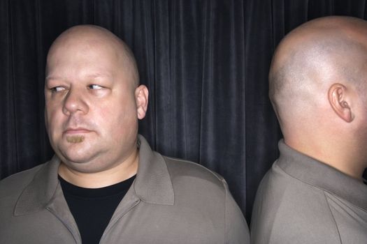 Caucasian mid adult bald man looking away from his identical twin.