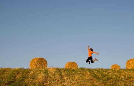 Woman jumping in a hay bales field