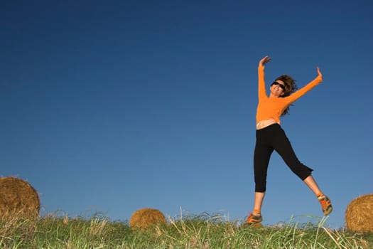 Woman jumping in a hay bales field