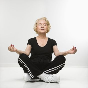 Caucasian senior woman sitting in yoga position on floor meditating.