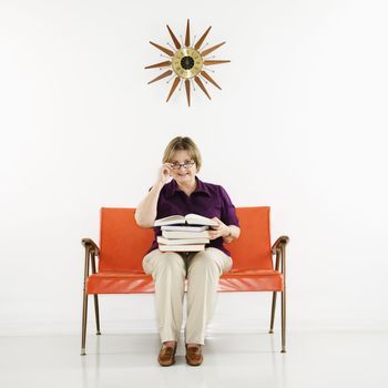 Caucasian middle aged woman sitting holding stack of books.