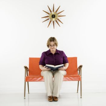 Caucasian middle aged woman sitting holding stack of books.