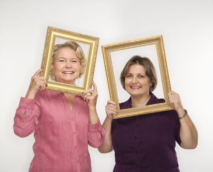 Caucasian middle aged woman and senior woman holding picture frames over faces.