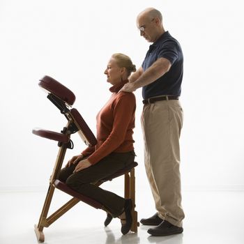 Caucasian middle-aged male massage therapist massaging shoulders of Caucasian middle-aged woman sitting in massage chair.