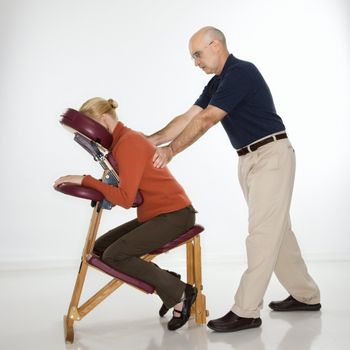 Caucasian middle-aged male massage therapist massaging back of Caucasian middle-aged woman sitting in massage chair.