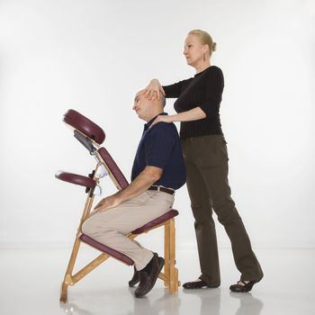 Caucasian middle-aged female massage therapist massaging neck of Caucasian middle-aged man sitting in massage chair.