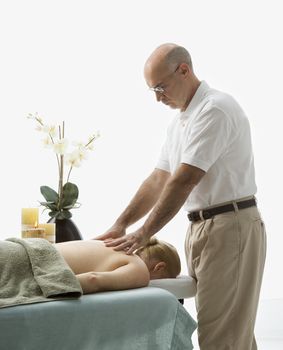 Caucasian middle-aged male massage therapist massaging back of Caucasian middle-aged woman lying on massage table.