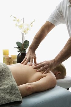 Caucasian middle-aged male massage therapist massaging back of Caucasian middle-aged woman lying on massage table.