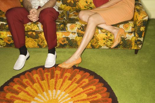 Female legs playing footsie with male legs by colorful retro sofa.