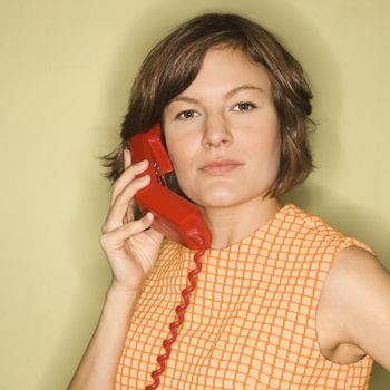 Head shot of pretty Caucasian mid-adult woman wearing orange dress listening to red telephone receiver.