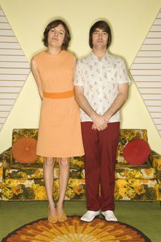 Caucasian mid-adult couple wearing retro clothes standing in room decorated with vintage furniture.