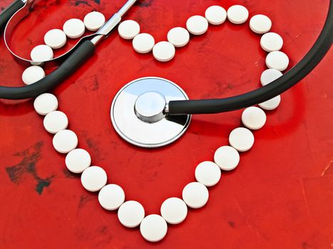 stethoscope and lot of pills over the red background