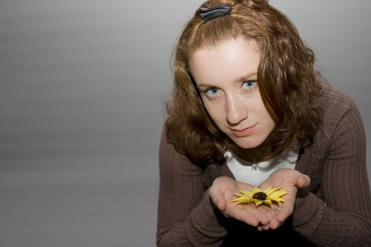 portrait of a beautiful redhaired girl holding a yellow flower in her hands