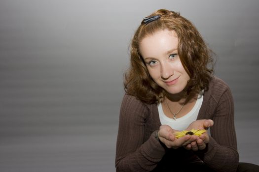 portrait of a beautiful redhaired girl holding a yellow flower in her hands