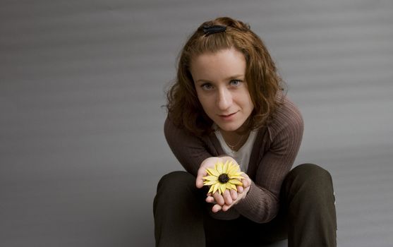 portrait of a beautiful redhaired girl holding a yellow flower in her hands