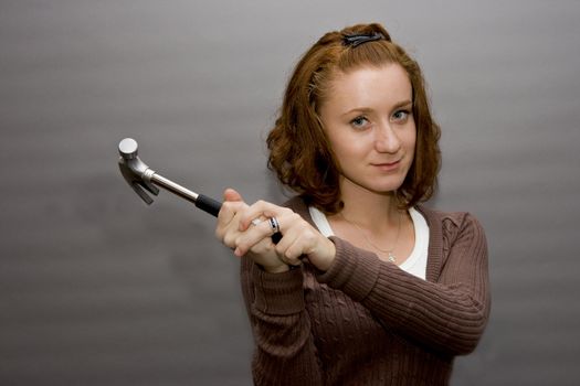 portrait of a beautiful redhaired girl holding a hammer. Be careful!