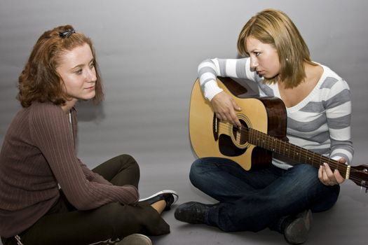 two girls. one girl playing guitar and the other one listening