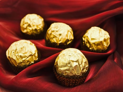 confection in golden candy wrapper at dark red textile  