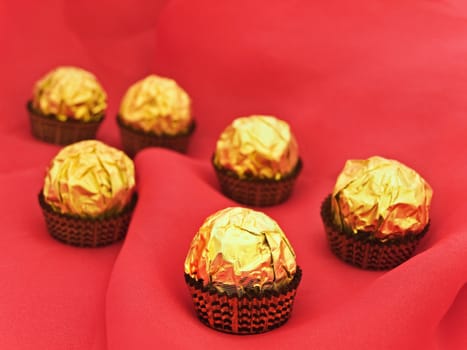 confection in golden candy wrapper at red textile background 