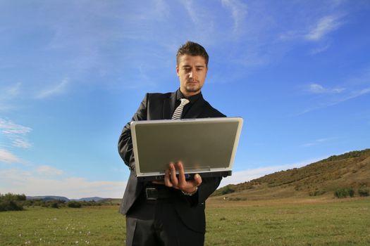 Typing on laptop in the middle of the field.