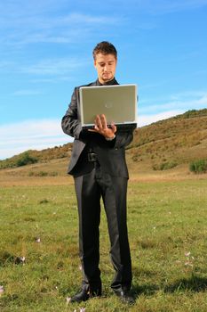 Standing person holding a laptop on a field.