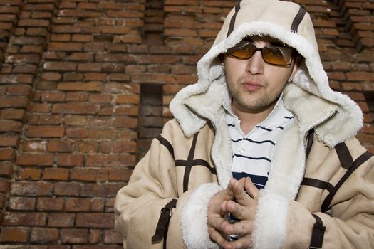 Rapper boy wearing a big leather coat posing in front of a brick wall
