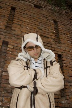 Rapper boy wearing a big leather coat posing in front of a brick wall