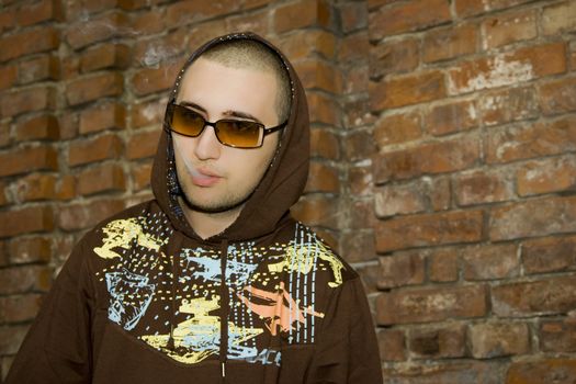 Rapper boy posing in front of a brick wall smoking