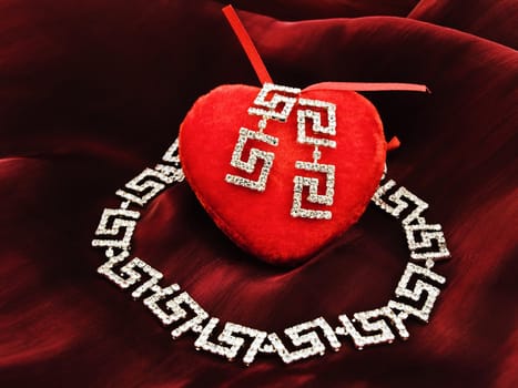 single red plush heart with jewelry over silk