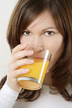 Photograph of a beautiful brunette drinking a glass of orange juice.