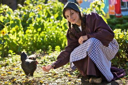 Young farm girl in traditional clothing feeding the chickens