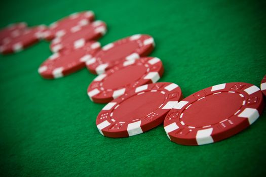 Line of red poker chips on green poker table.