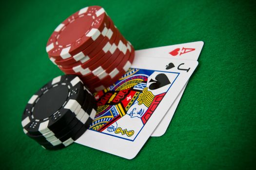 Ace of hearts and black jack with stack of black and red poker chips on green table.
