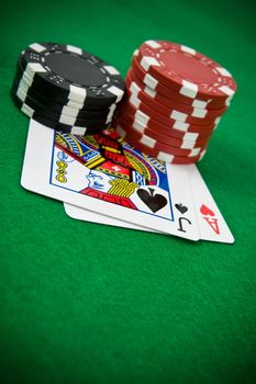 Ace of hearts and black jack with stack of black and red poker chips on green table.