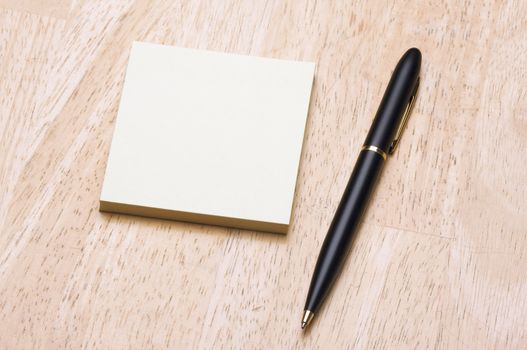 Pen and Post It Notes Pad Against a Wood Background