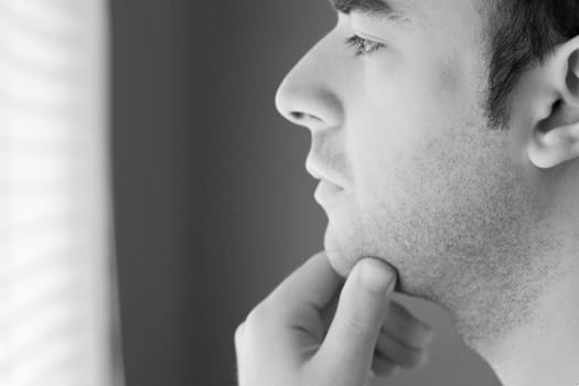 A young man with his hand on his chin thinking an important decision - black and white.