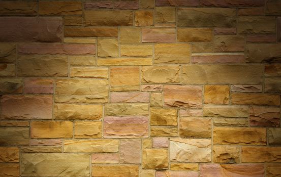 Pink and gold masonry wall with irregular size rectangular stones dramatically lit from above