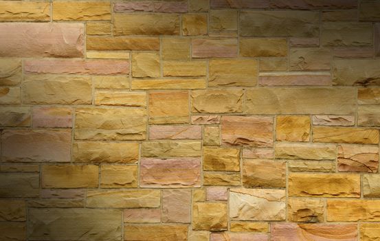 Pink and gold masonry wall with irregular size rectangular stones dramatically lit diagonally