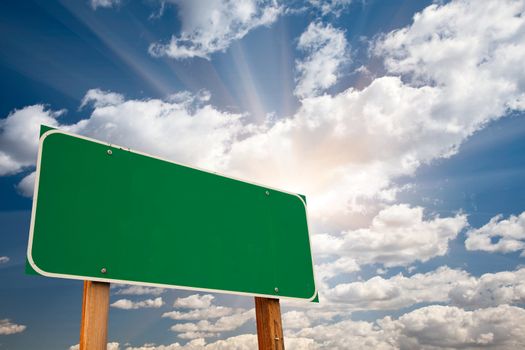 Blank Green Road Sign over Dramatic Blue Sky with Clouds and Sunburst - Ready for your own message and Room For Copy on Clouds.