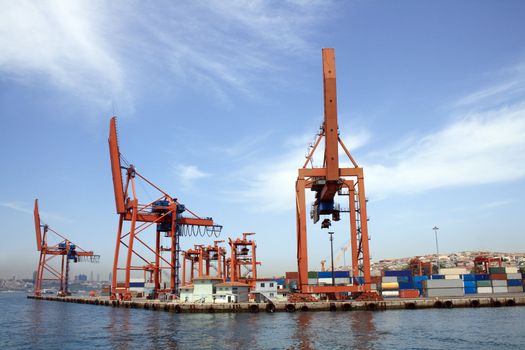 Panorama with blue sky, sea and container harbour. Closeup of few red cranes