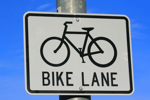 Bike lane road sign over blue sky.
