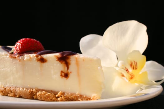Cheesecake and a white orchid on a plate with a black background.