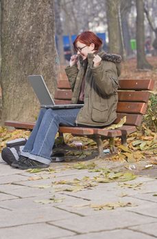 Happy redheaded girl with a laptop in an autumn park.