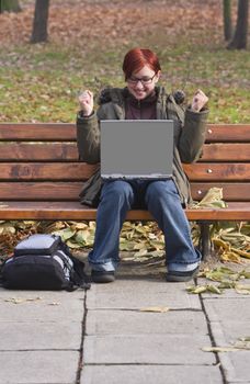 Happy redheaded girl with a laptop in an autumn park.
