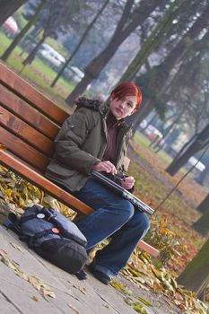 Lonely girl with a laptop siting on a bench in an autumn park.
